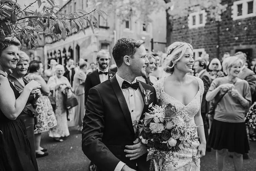 Black-and-white photograph of the couple smiling among wedding guests outdoors.