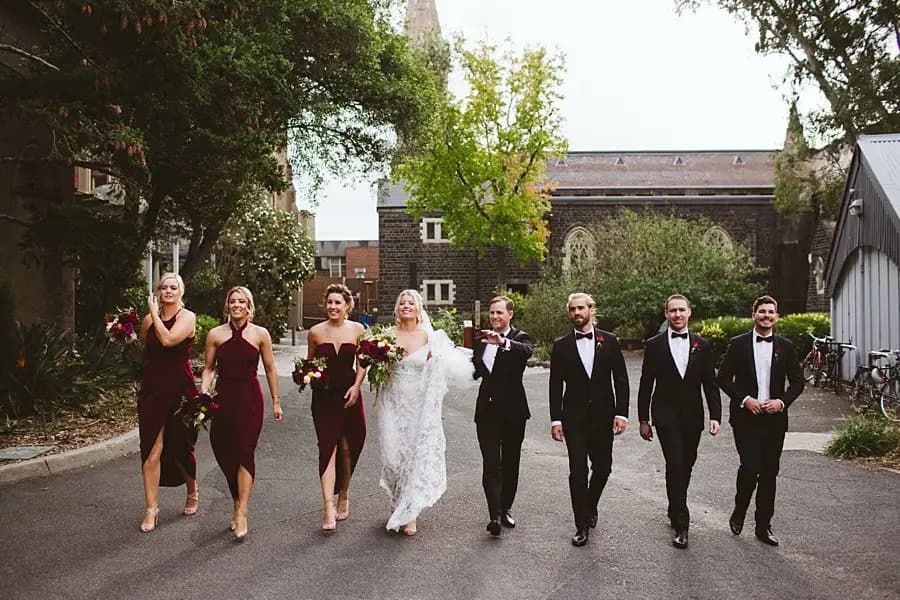 Wedding party walking together along a tree-lined paved path.