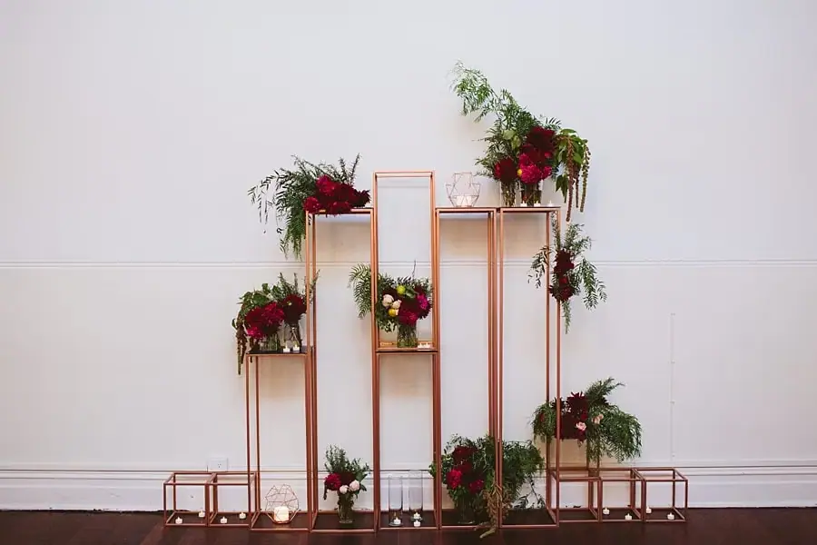 Flowers arranged on tall copper-colored stands against a white wall.