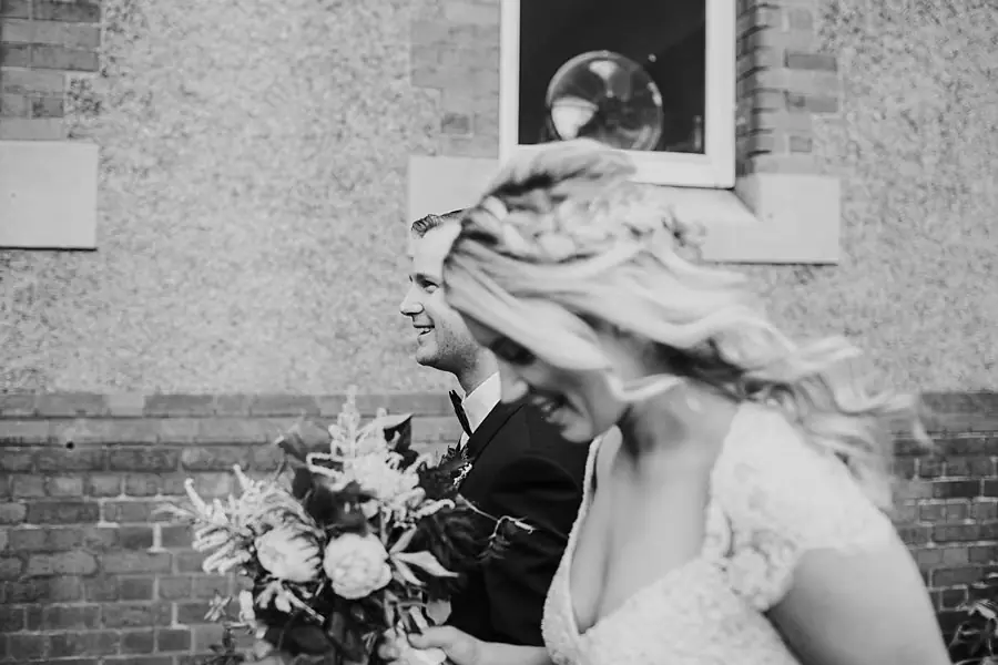 Black-and-white photograph of the laughing couple with the bride's hair blowing sideways.