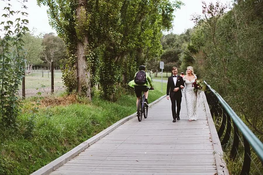 Couple walking along a wooden bridge beside a passing cyclist.