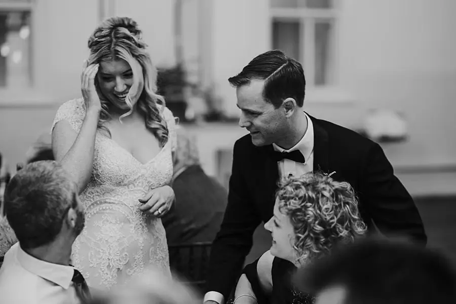 Black-and-white photograph of the bride and groom greeting seated guests.