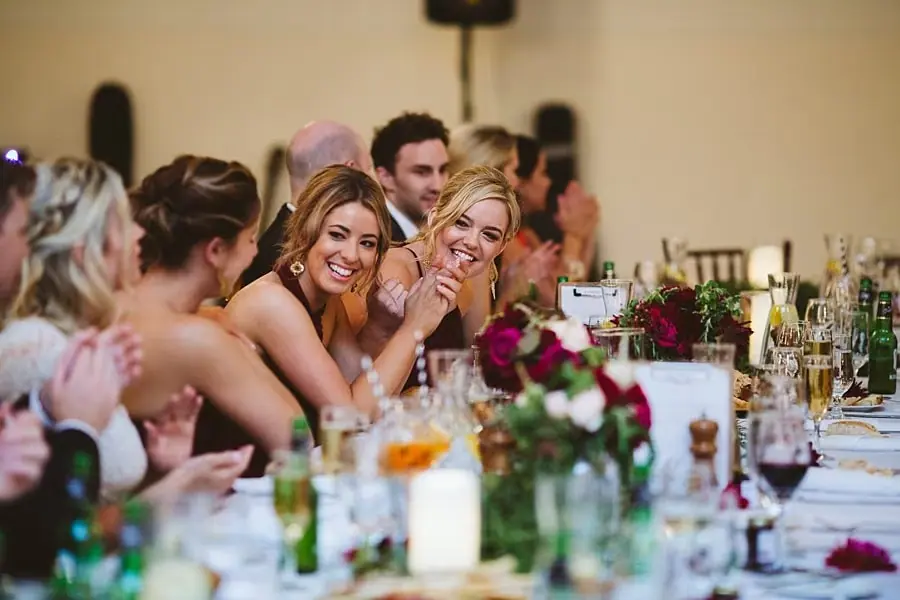 Women smiling together at a flower-decorated reception table.