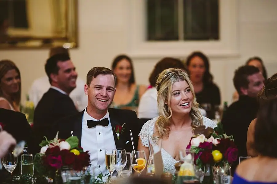 Bride and groom smiling while seated at their reception table.