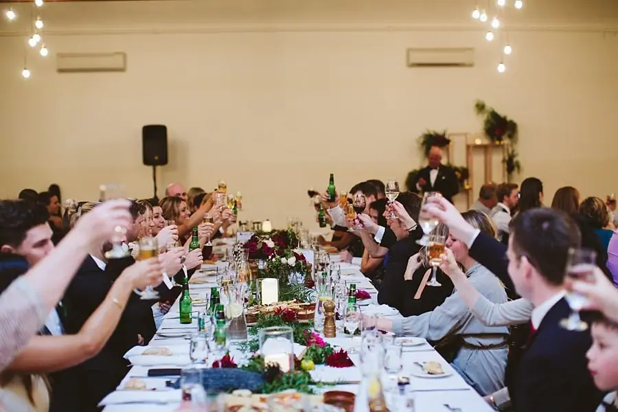 Wedding guests raising glasses over a long reception table.