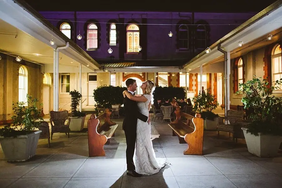 Bride and groom embracing in a warmly lit courtyard at night.