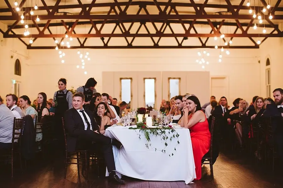 Guests watching a speaker across a decorated reception table.