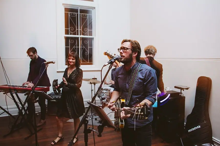 Band performing with guitar, keyboard and microphones indoors.