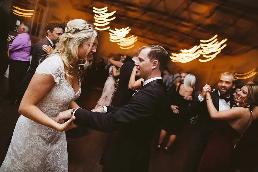 Bride and groom holding hands and dancing among wedding guests.