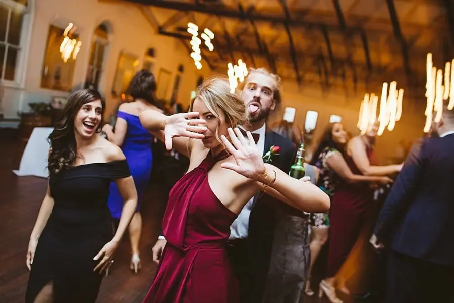 Woman in a burgundy dress raising her hands while dancing with friends.