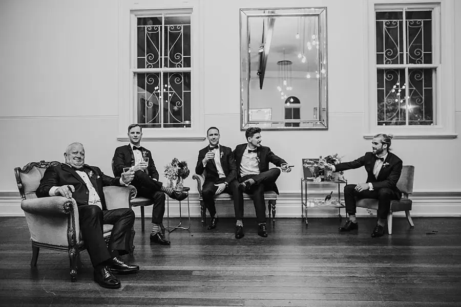 Black-and-white photograph of five suited men seated in a row of chairs.