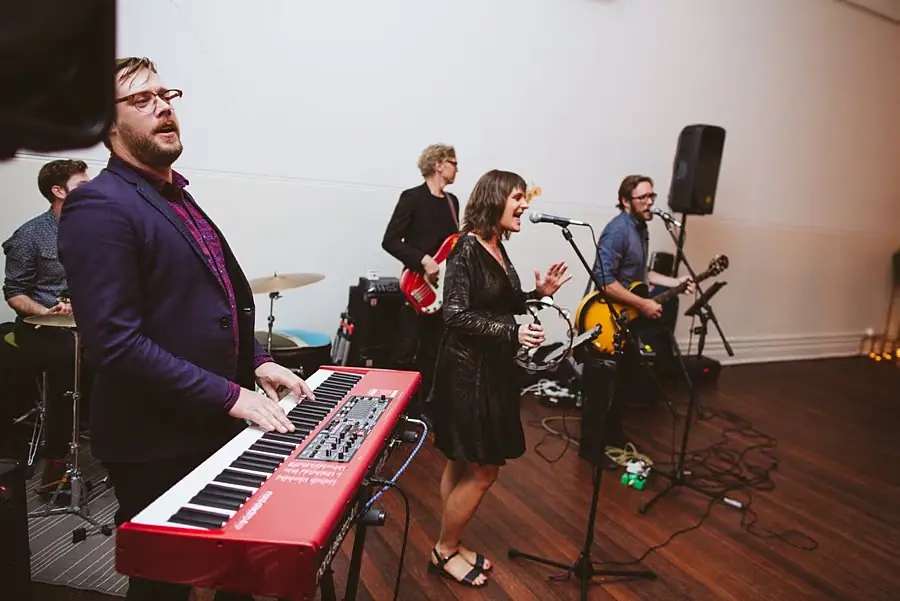 Keyboard player in the foreground with a singer and guitarist performing behind him.