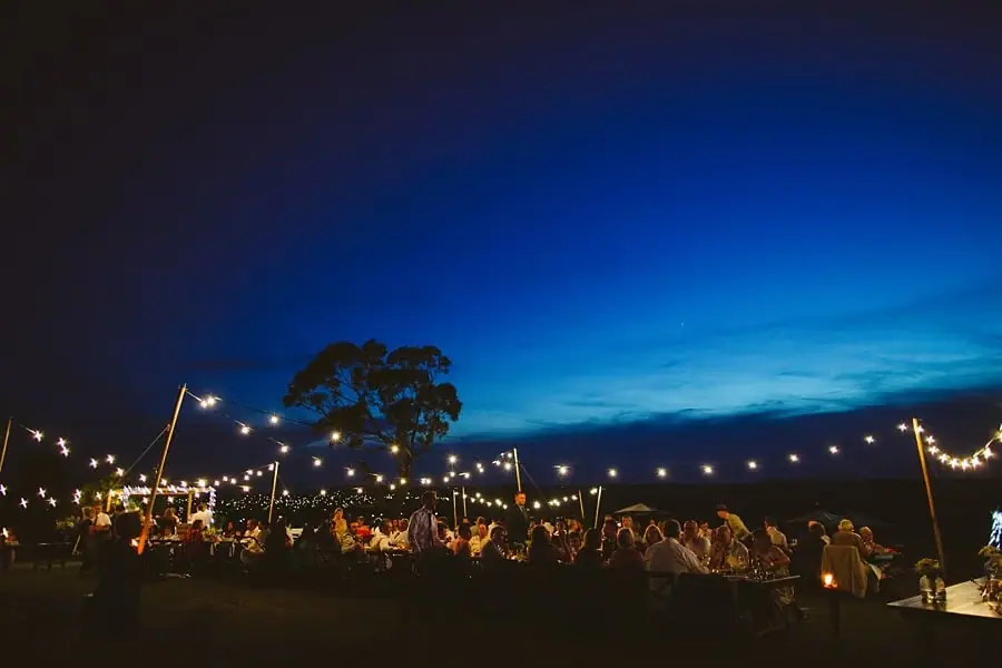 Guests seated at the outdoor reception beneath festoon lights at dusk