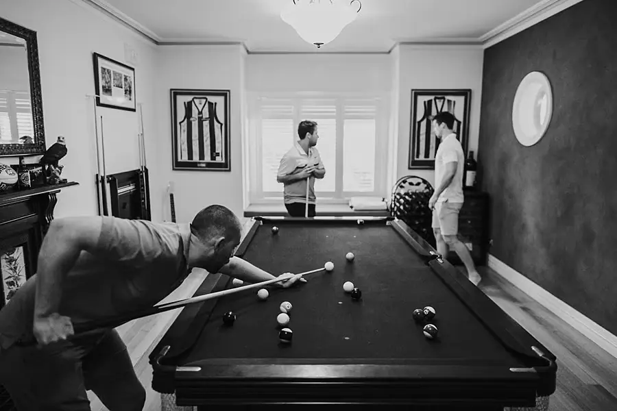 Black-and-white photograph of men playing pool in a room with framed pictures.