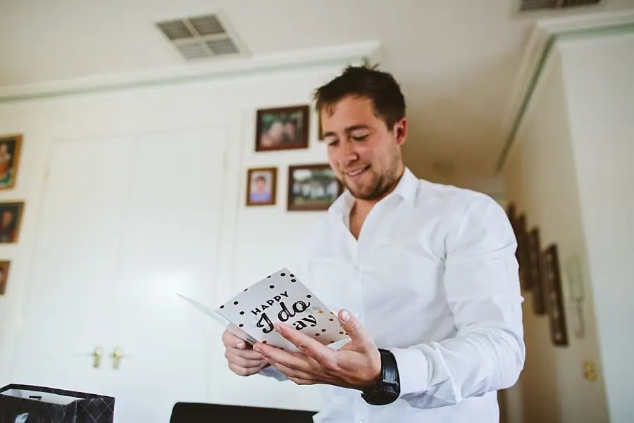 Man in a white shirt smiling while reading a card.