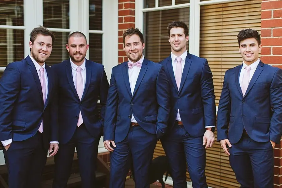 Five men in navy suits posing outside a brick house.