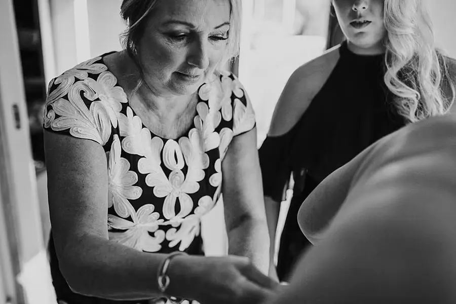 Black-and-white close-up of a woman helping adjust the bride's clothing.
