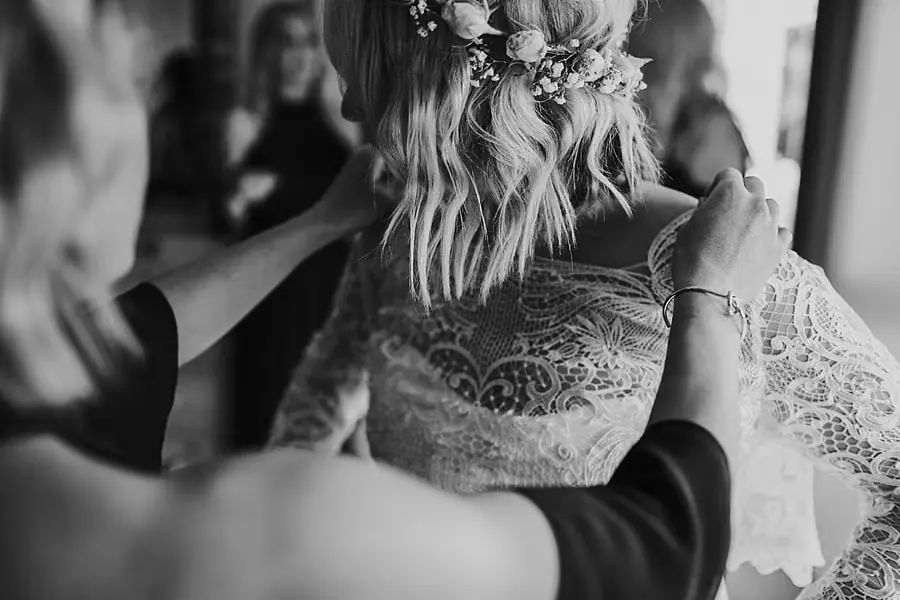 Black-and-white close-up of hands adjusting the bride's lace neckline.