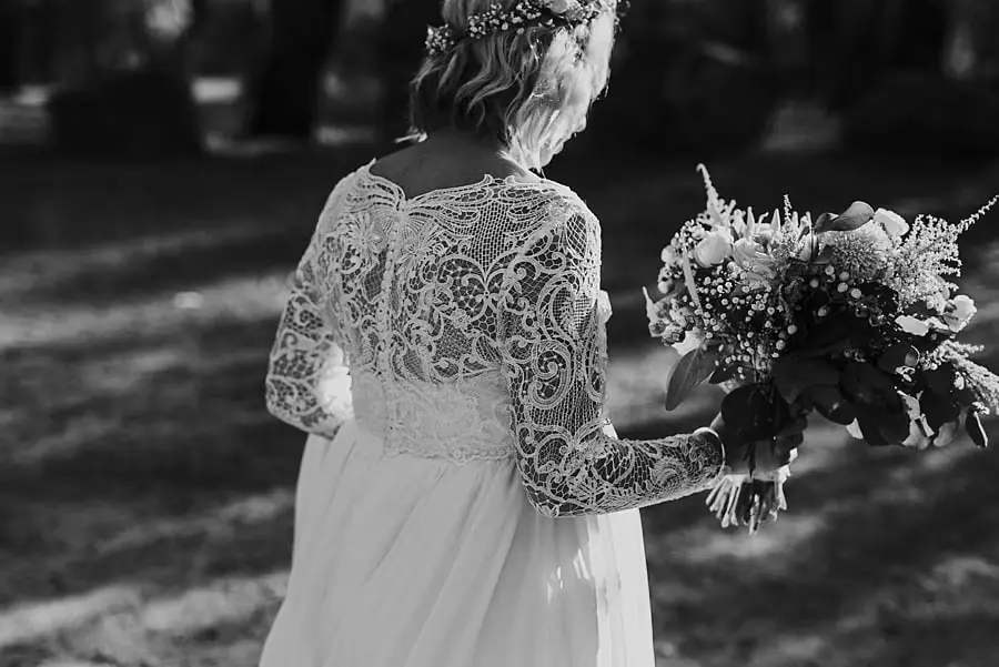 Black-and-white photograph of the bride holding her bouquet in woodland.