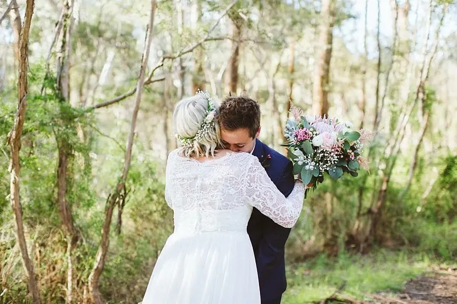 Bride and groom embracing among tall slender trees.
