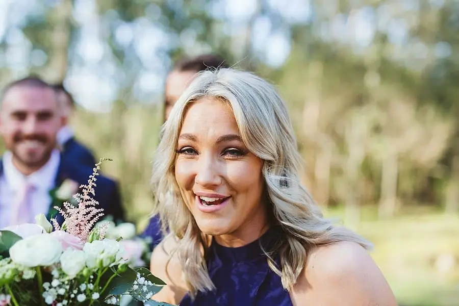 Woman in a purple dress smiling with a bouquet in woodland.