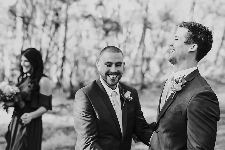 Black-and-white photograph of two suited men laughing in woodland.