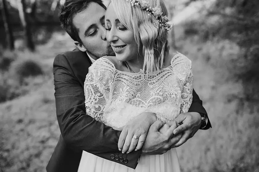 Black-and-white close-up of the groom kissing the bride's cheek from behind.