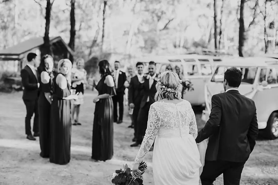 Black-and-white photograph of the couple approaching their wedding party beside a van.