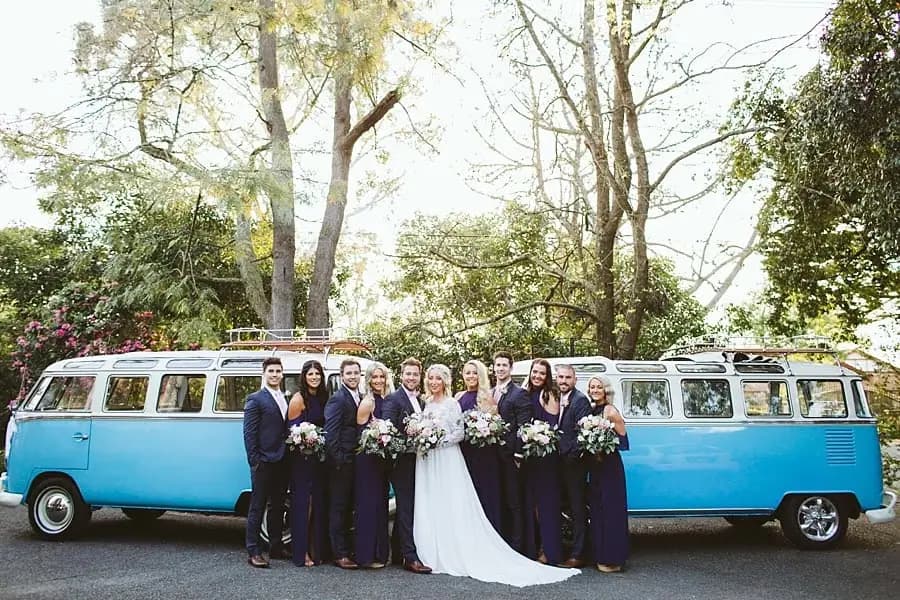 Wedding party posing between two blue and white vintage vans.