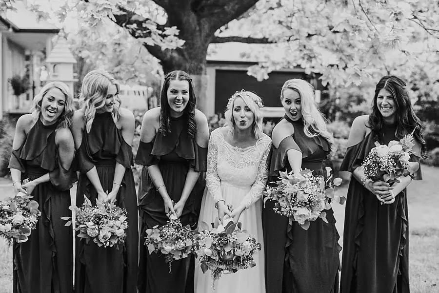 Black-and-white photograph of the bride and five women holding bouquets outdoors.