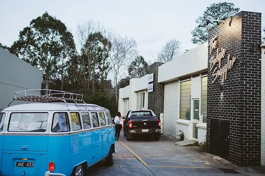 Blue and white vintage van parked outside a low brick building.
