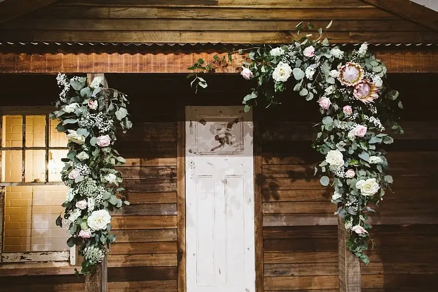 Pale pink and white flowers framing a timber ceremony backdrop.