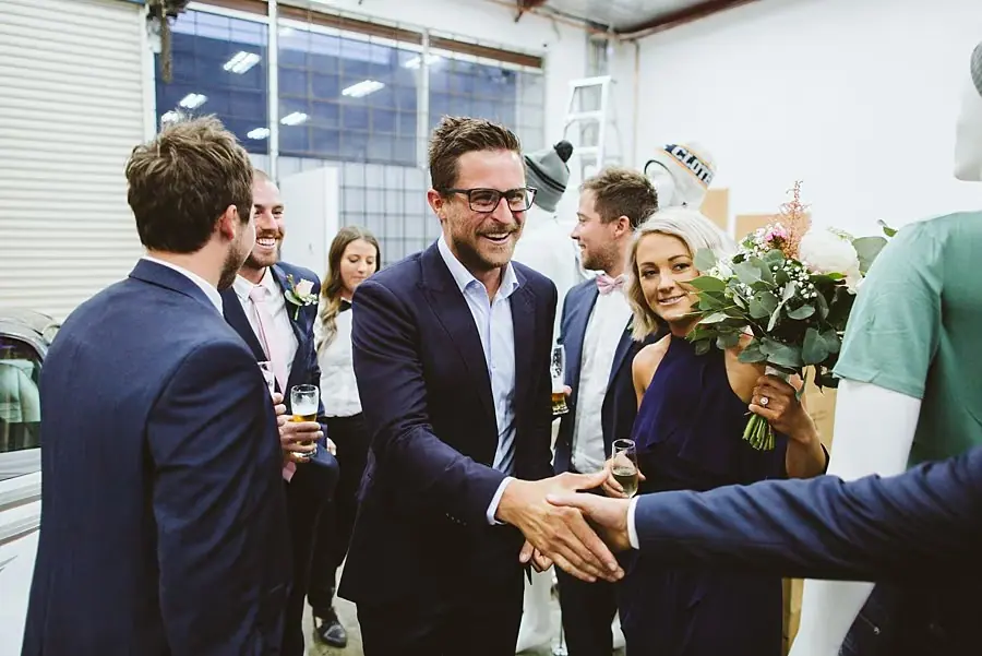 Wedding guests greeting one another indoors with drinks.