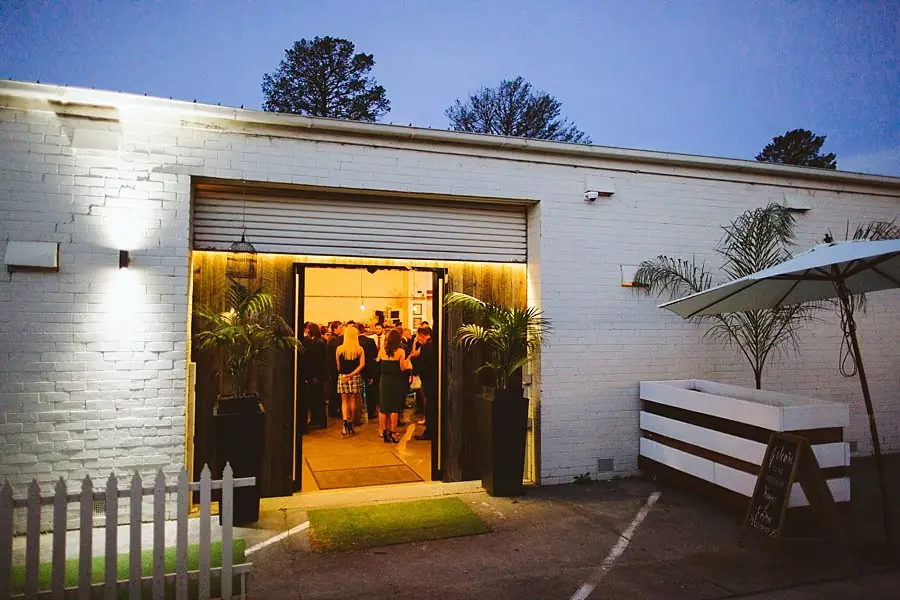 Guests visible through an open doorway in a white brick building at dusk.