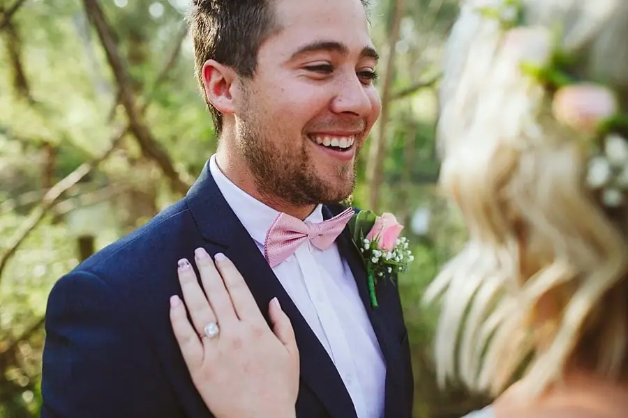 Groom smiling toward the bride as her ringed hand rests on his jacket.