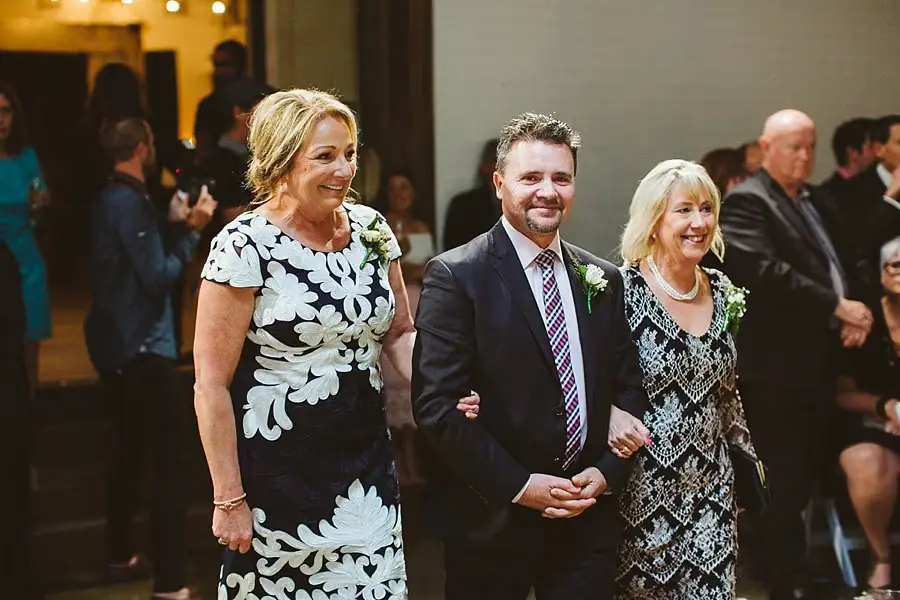 Three guests standing together and smiling toward the ceremony.