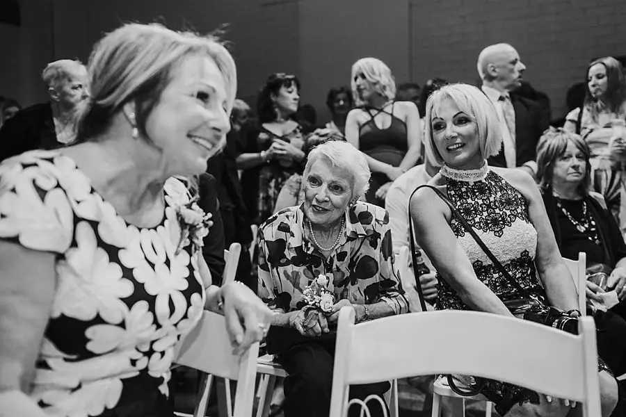 Black-and-white photograph of guests smiling from ceremony seats.