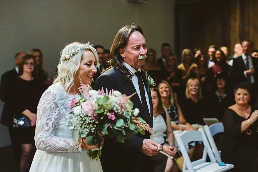 Bride walking beside a suited man while guests look on.
