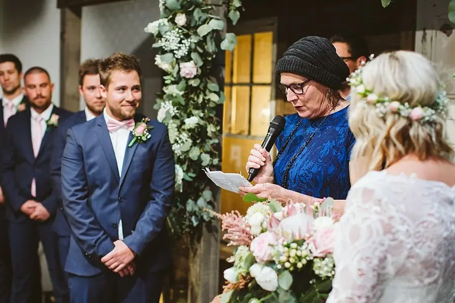 Woman reading from a sheet into a microphone beside the couple.