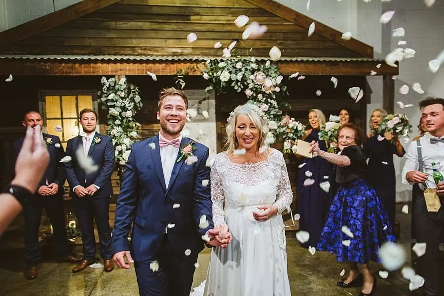 Bride and groom walking hand in hand as guests scatter flower petals.