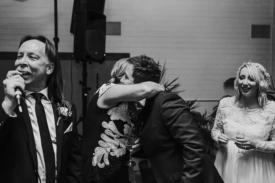 Black-and-white photograph of the bride embracing a suited man beside a speaker.