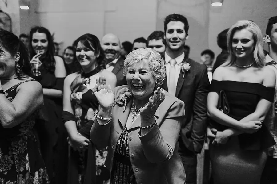 Black-and-white photograph of an older guest gesturing excitedly among smiling people.