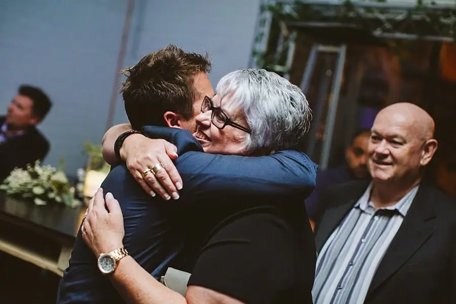 Suited man embracing a gray-haired woman among reception guests.
