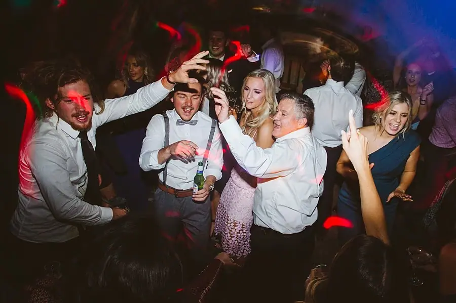 Guests dancing together beneath colorful reception lights.