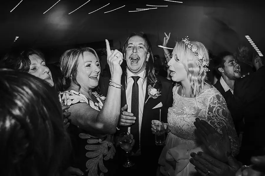 Black-and-white photograph of the bride and guests singing and gesturing together.
