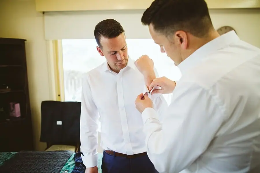 Man fastening a cuff while another man in a white shirt stands beside him.