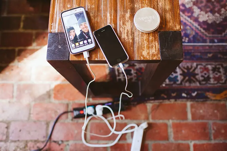 Mobile phones and charging cables resting on a wooden surface, with a video call visible on one screen.