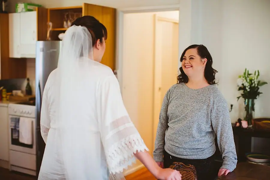 Veiled bride holding hands with a smiling woman indoors.