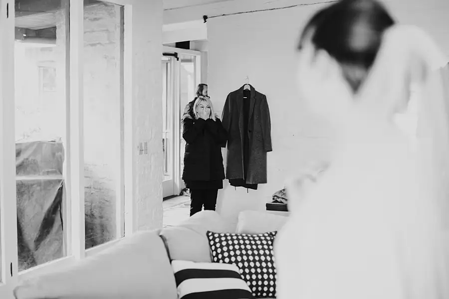 Black-and-white photograph of women preparing in a living room, reflected in a mirror.