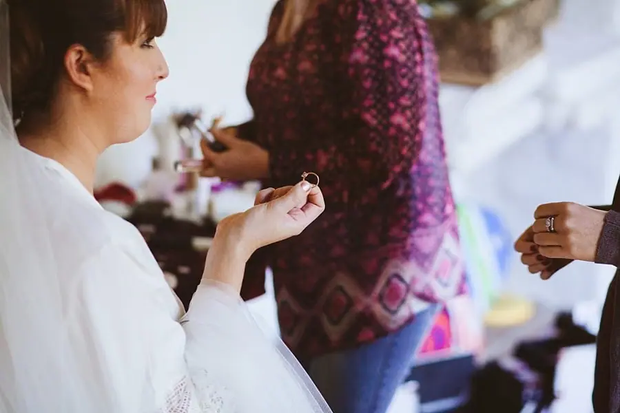 Bride in a white robe holding a small piece of jewellery during preparations.